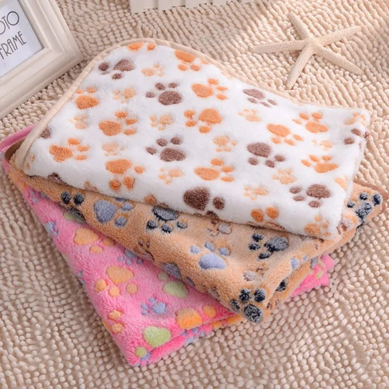 Close-up of pink, beige, and white ultra-soft fleece pet blankets with multicolored paw print patterns.