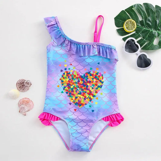 One-piece girl's swimsuit with purple and blue fish scale patterns, a colorful heart mosaic, and hot pink ruffles.
